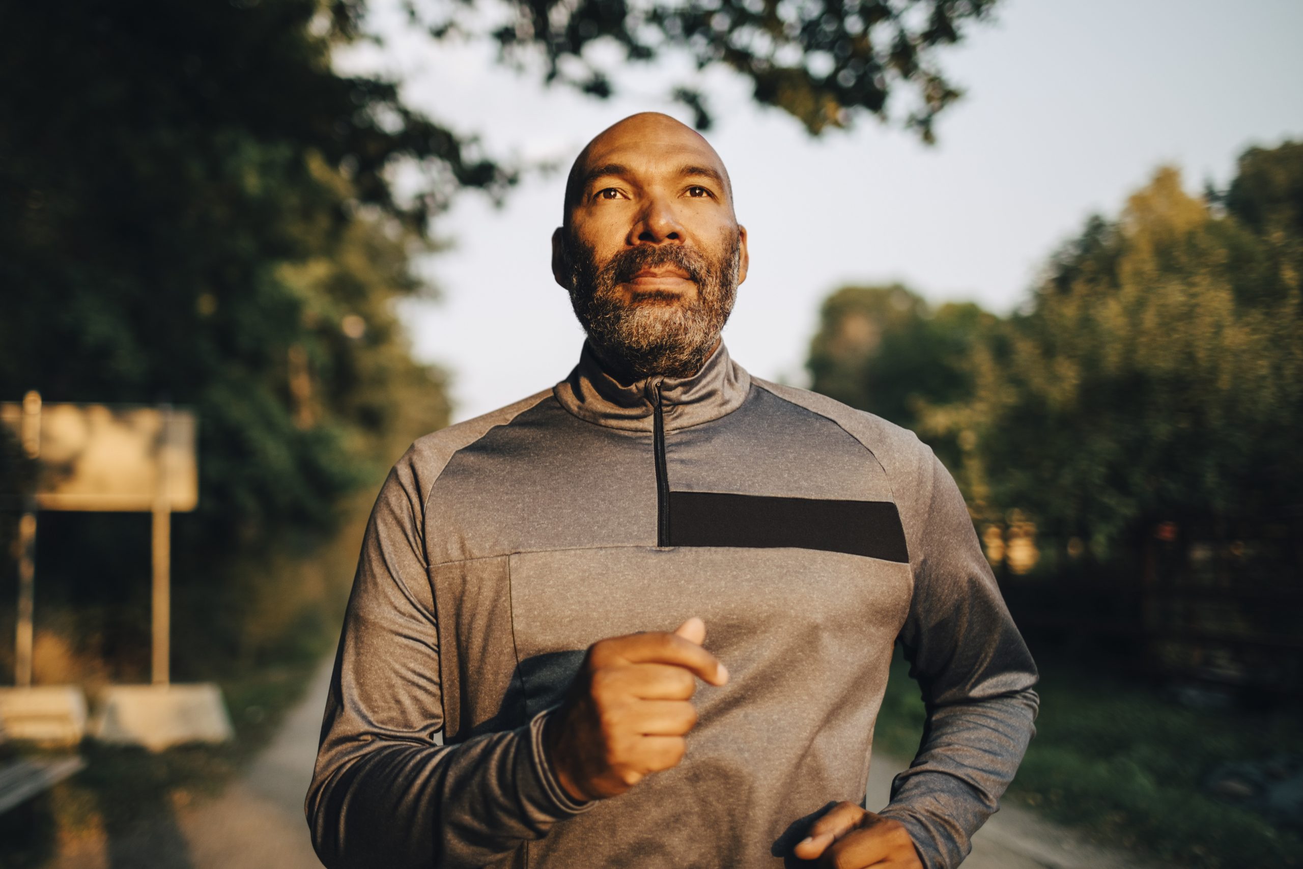 Confident mature man looking away while jogging in park during sunset